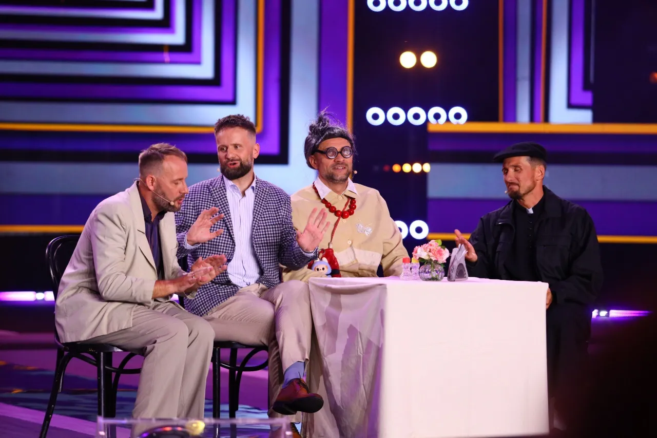 Czterech panów, w tym jeden przebrany za kobietę, siedzi przy stole. To chyba kabaret z Kielc, który rozbawia publiczność.