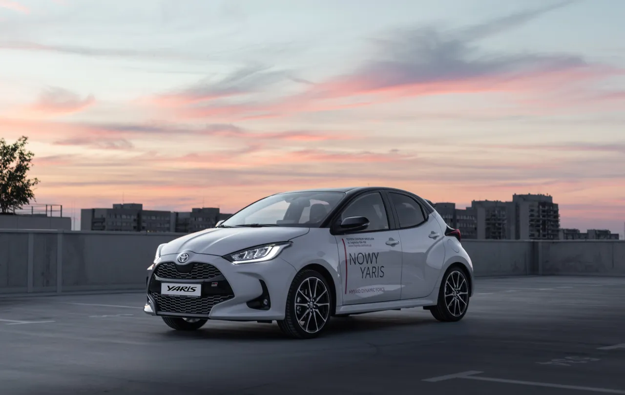 Nowy Toyota Yaris GR Sport na parkingu, z zachodem słońca w tle. Zastanawiasz się, ile koni ma Toyota Yaris? Ten model oferuje dynamiczne osiągi.