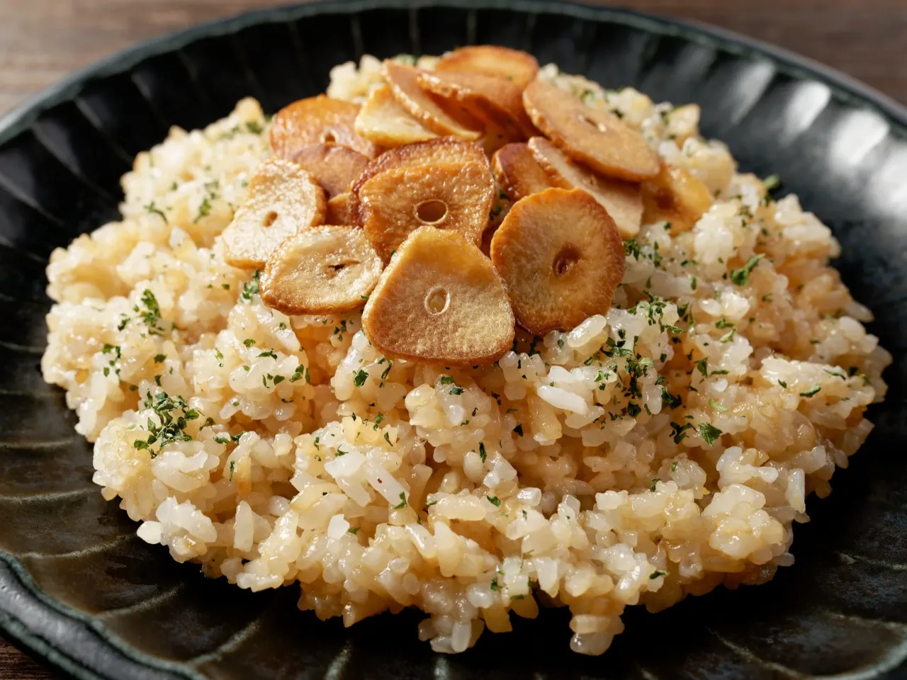 Pyszny ryż smażony z chrupiącym czosnkiem i posiekaną natką pietruszki, podany na czarnym talerzu.