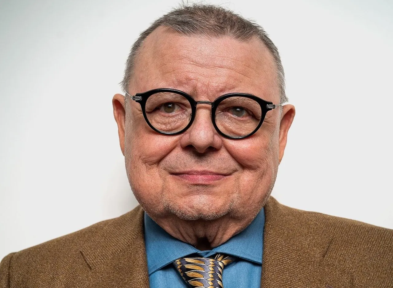 Uśmiechnięty Wojciech Mann w okularach i brązowej marynarce. Zastanawiasz się, ile lat ma Wojciech Mann?