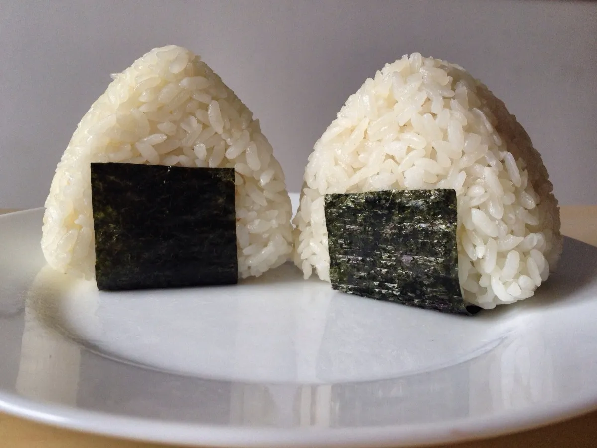 Dwa pyszne onigiri z ryżu, ozdobione kawałkami nori, gotowe do spożycia.