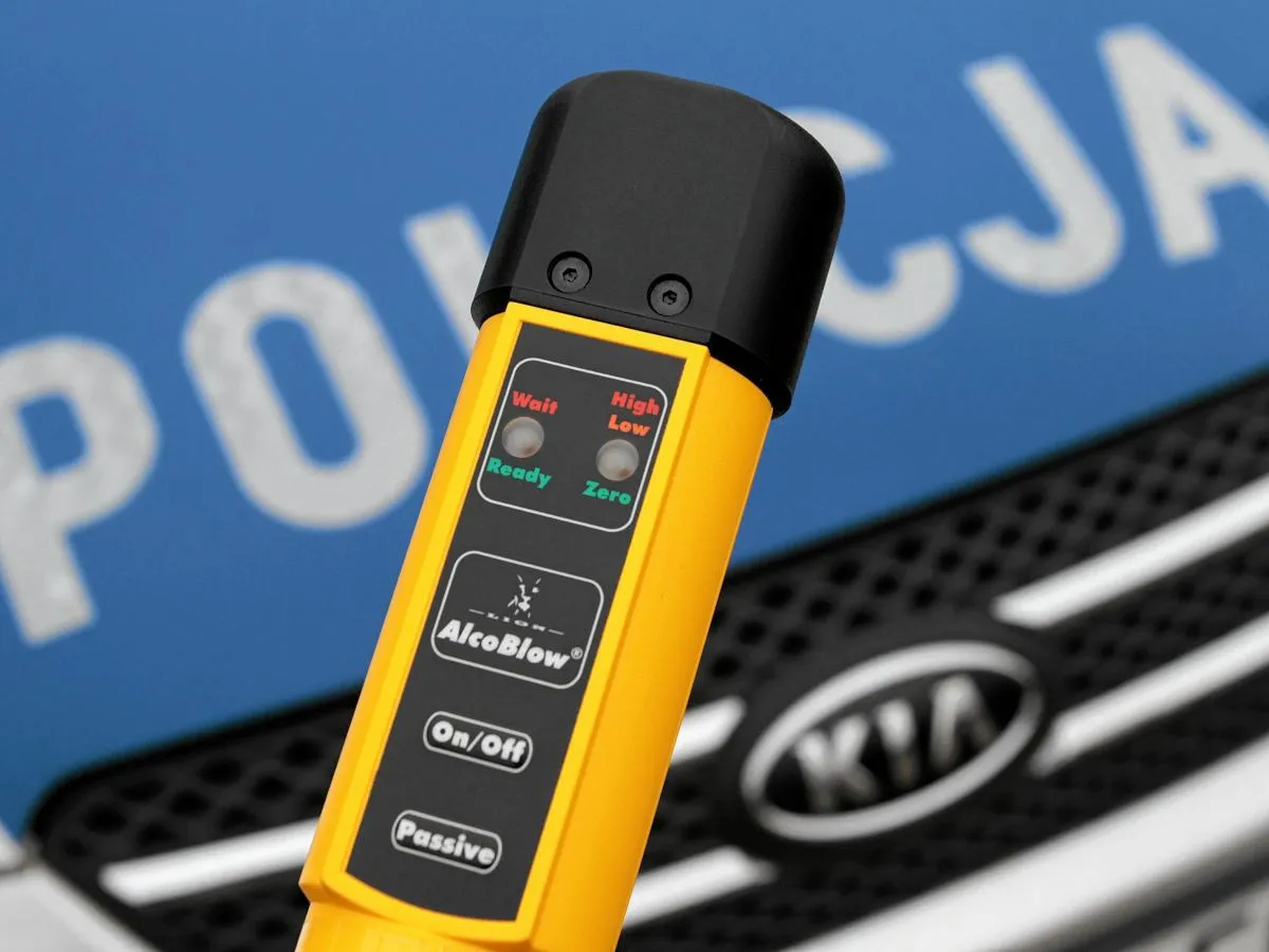 Alkomat policyjny na tle radiowozu. Sprawdź, ile możesz wypić, zanim wsiądziesz za kierownicę.