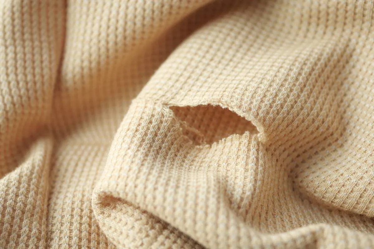 Dziura w beżowym swetrze, idealna do nauki, jak zacerować sweter.