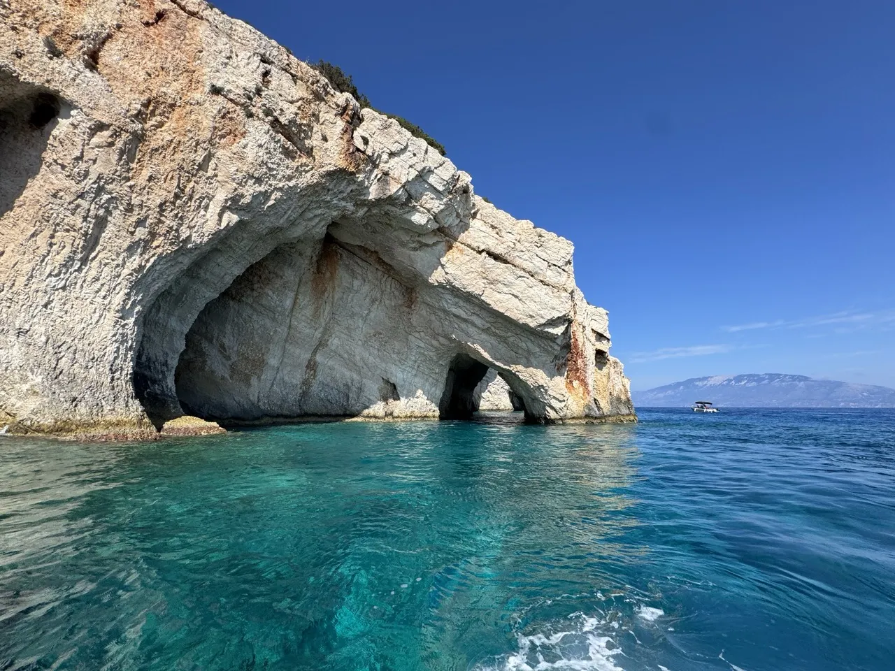 Turkusowe wody i skalne jaskinie - to jedne z zakynthos najpiękniejsze miejsca. Mała ł&oacute;dka na horyzoncie.