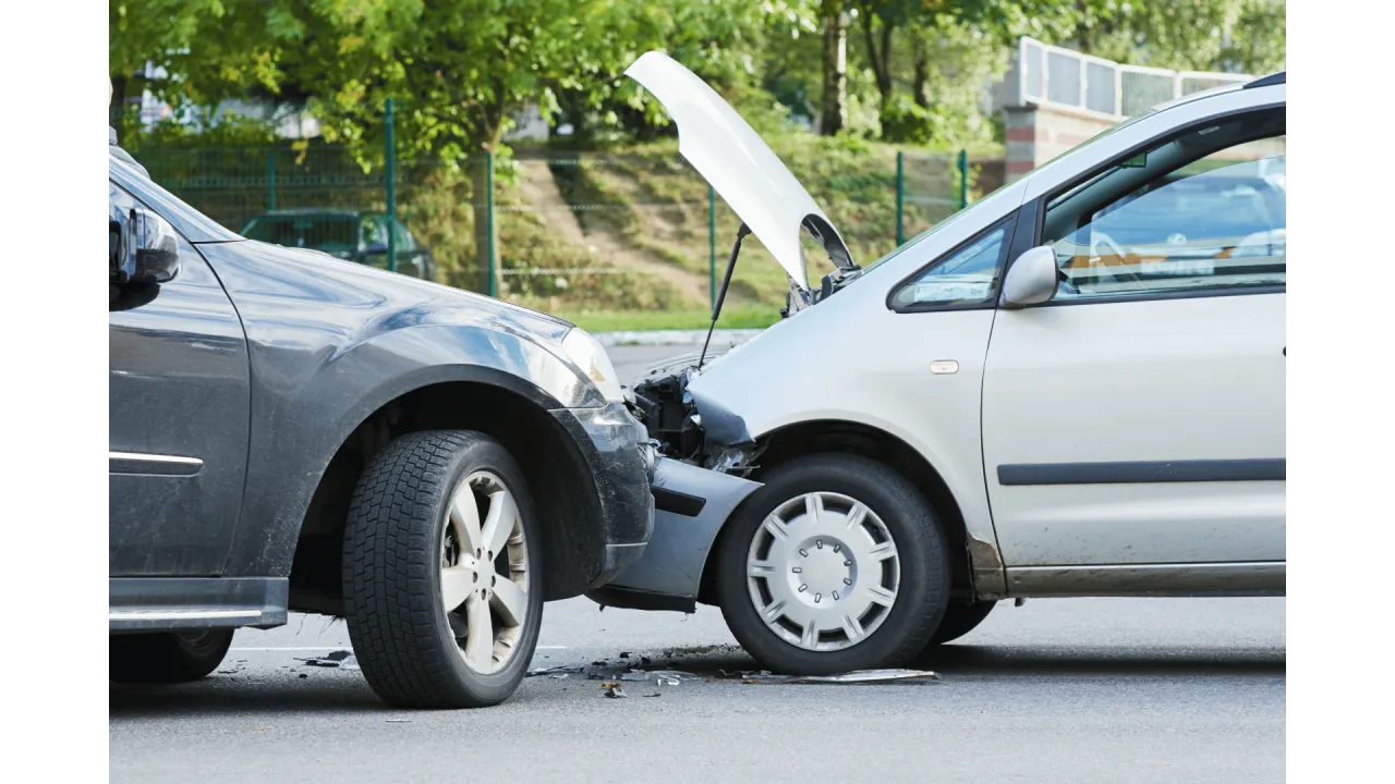Dwa samochody po kolizji, jeden srebrny z otwartą maską, drugi ciemny. Widoczna szkoda majątkowa na obu pojazdach.