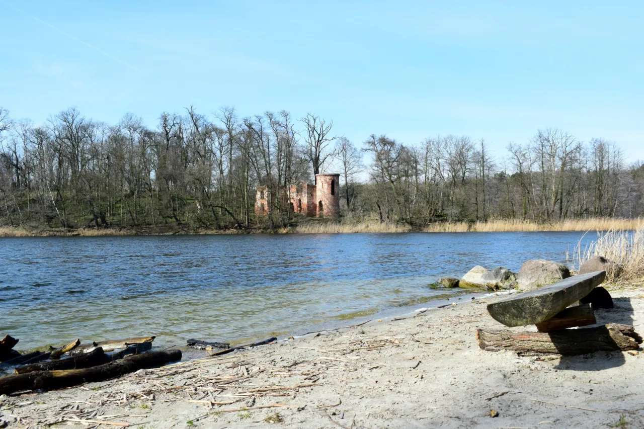 Ruiny zamku nad jeziorem, idealne miejsce, by zobaczyć, co zwiedzić w Ełku. Piękny krajobraz z ławką z drewna na pierwszym planie.