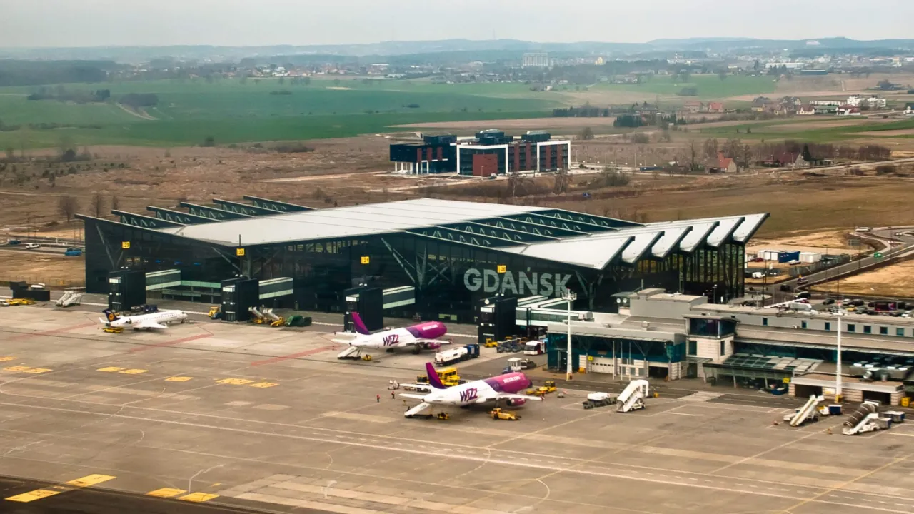 Nowoczesny terminal lotniska w Gdańsku z samolotami Wizz Air na płycie. W tle pola i zabudowania.