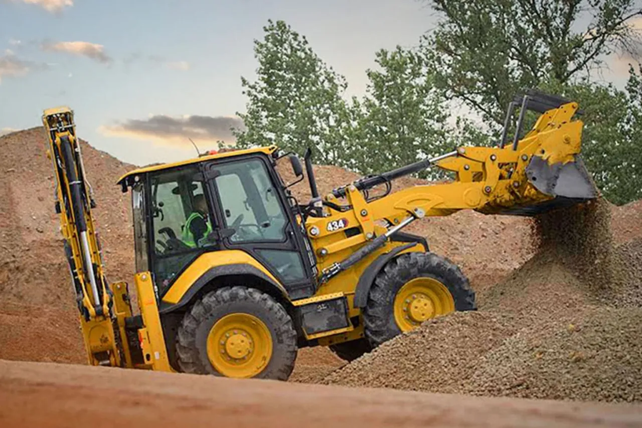 Koparko-ładowarka z uprawnieniami na koparko ładowarkę pracuje na budowie, przesypując żwir.