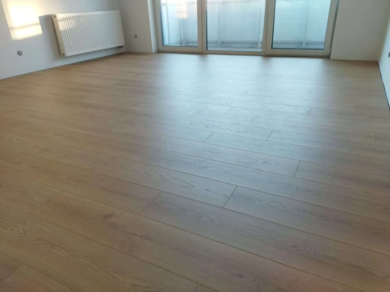 Nowe panele ułożone równolegle do okna, tworząc jasną i przestronną przestrzeń. Wskazówka: jak układać panele kierunek ma znaczenie dla optycznego powiększenia pomieszczenia.