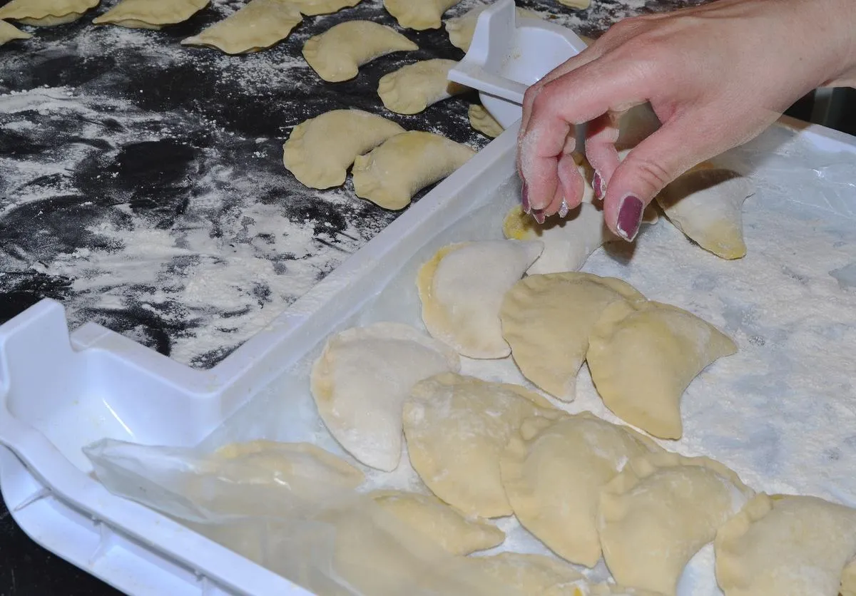 Ręka układa pierogi w pojemniku, posypane mąką, by ugotowane pierogi się nie skleiły.