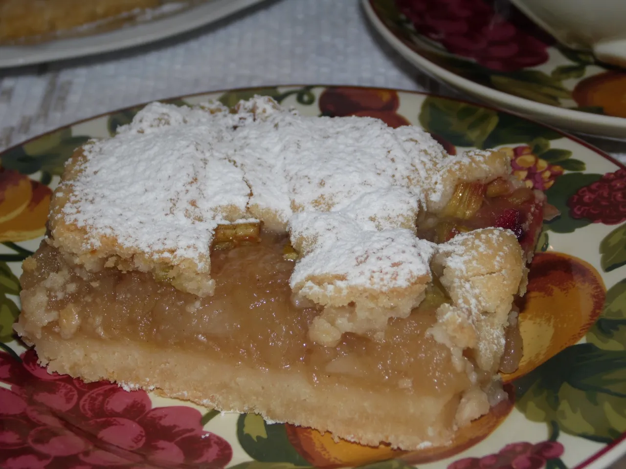 Kawałek kruchego ciasta z jabłkami, posypany cukrem pudrem. Czy do kruchego ciasta daje się proszek do pieczenia? To pytanie nurtuje wielu piekarzy.