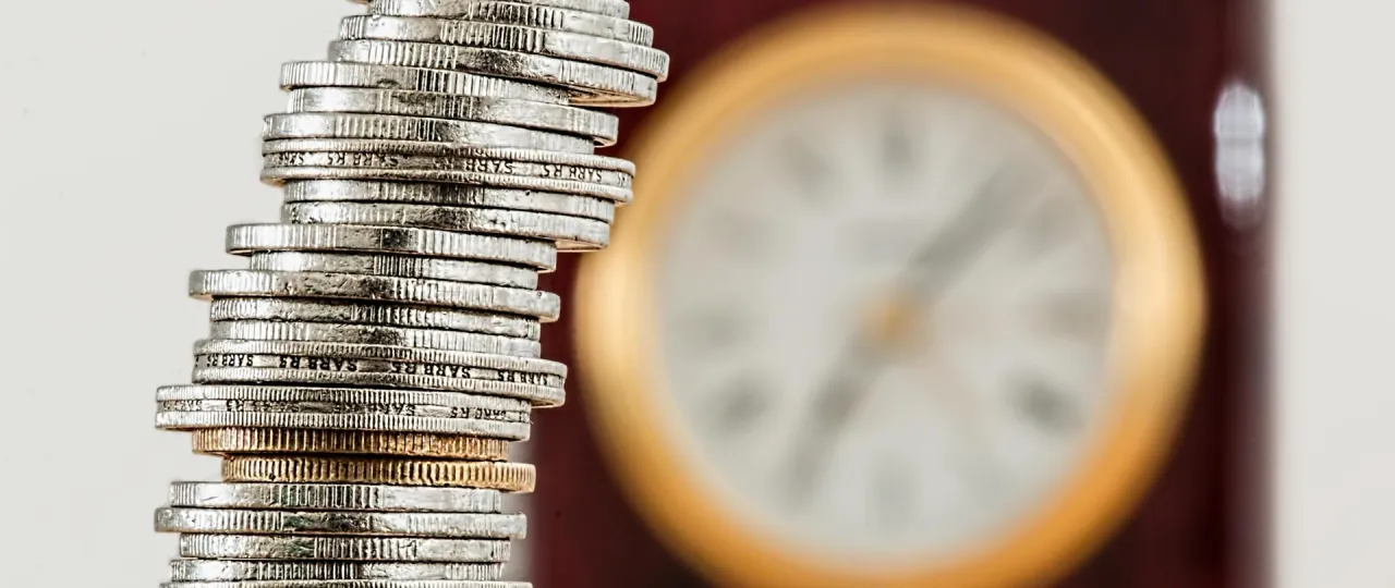 Stos monet i zegar w tle. Kiedy długi stają się przytłaczające, upadłość konsumencka dla kogo jest szansą na nowy start.