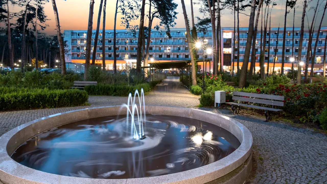 Wieniec-Zdrój sanatorium: malowniczy park z fontanną i ławkami, oświetlony budynek hotelowy. Sprawdź ceny pobytu!