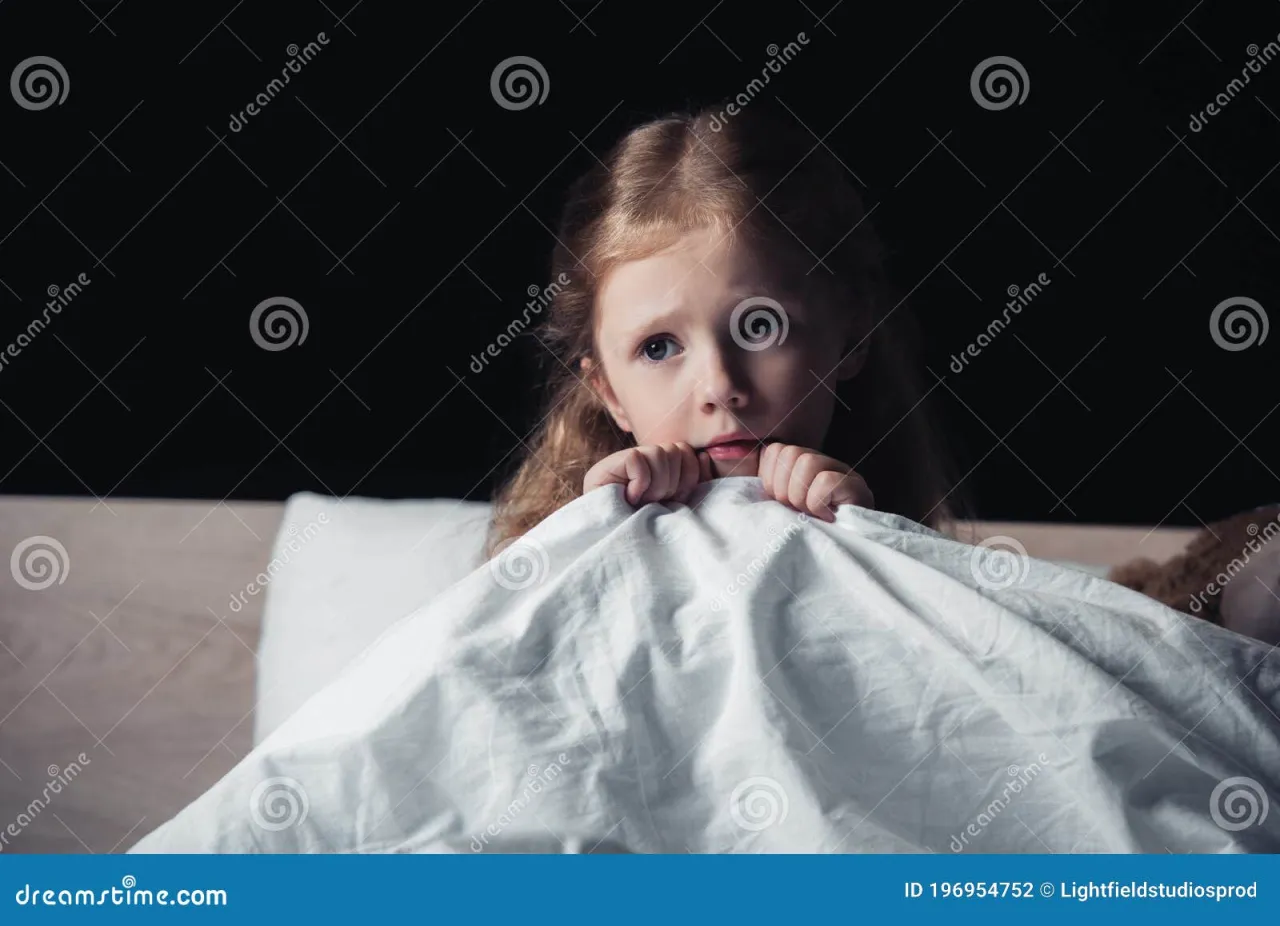 dziecko siedzące na łóżku w nocy, wyglądające na przestraszone