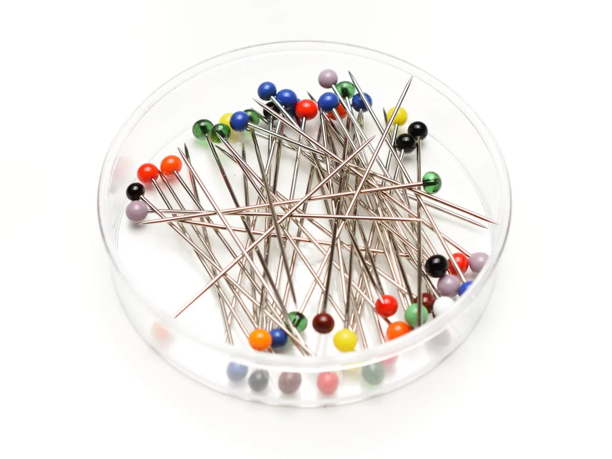 Kolorowe gł&oacute;wki szpilek w przezroczystym pojemniku, gotowe do pracy krawieckiej.