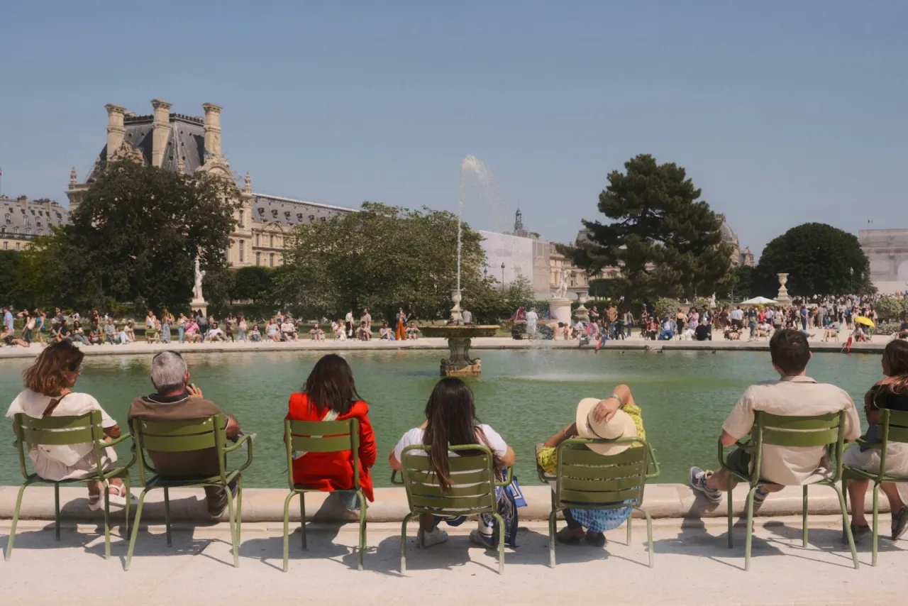 Relaks w paryskim ogrodzie, idealny pomysł, co robić w Paryżu w sierpniu. Ludzie odpoczywają przy fontannie, podziwiając Luwr.
