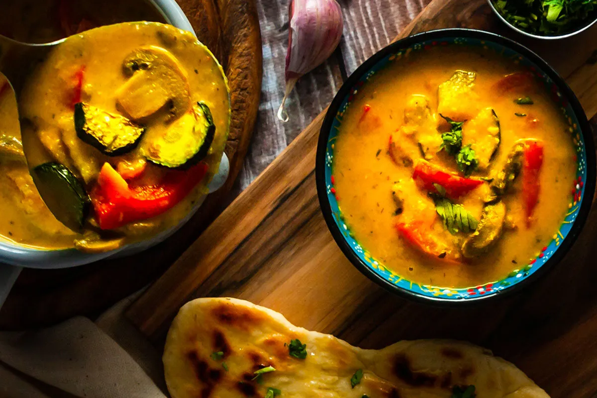 Aromatyczne tajskie curry z warzywami, podane w misce i chochli, obok chlebka naan i czosnku.