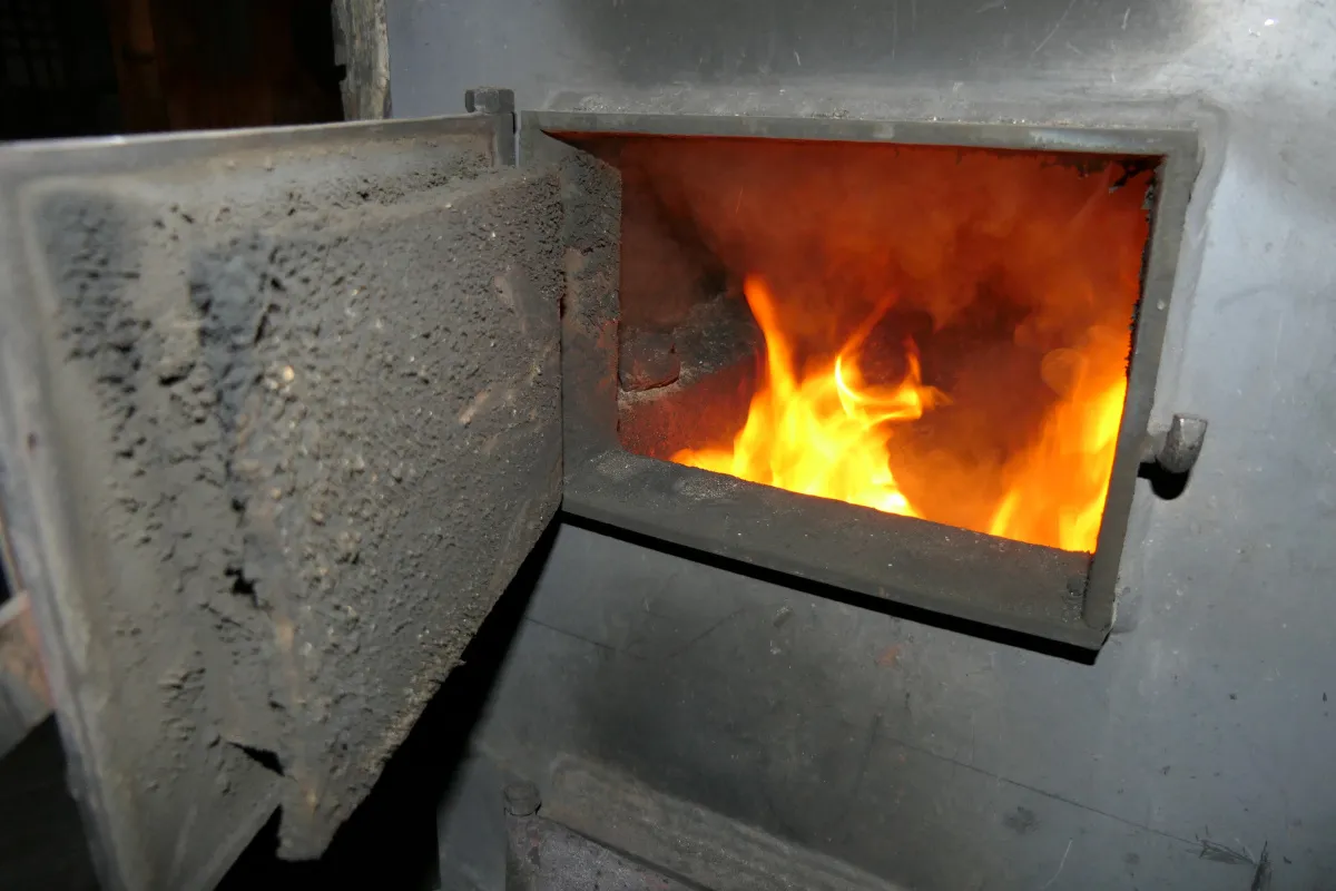 Jasne płomienie tańczą w palenisku pieca bezklasowego. Otwarta, okopcona klapa dodaje surowego uroku.