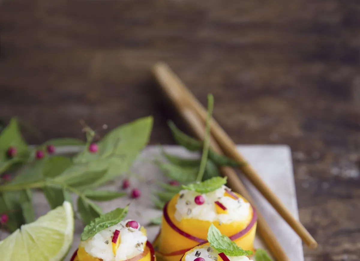 Wykwintne sushi z mango, ryżem i owocami, ozdobione miętą i granatem. Obok limonka i pałeczki.