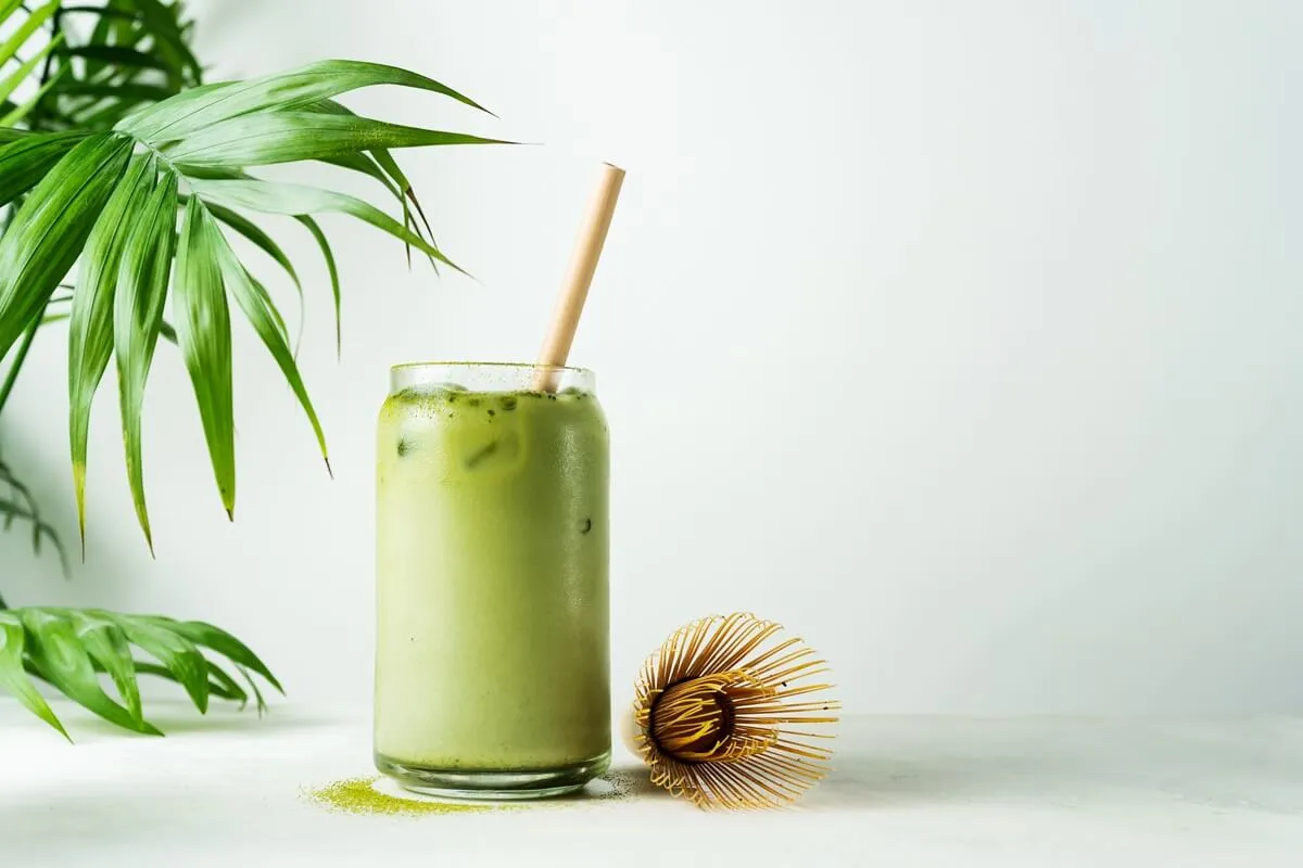 Orzeźwiające matcha latte z lodem i bambusową słomką, obok bambusowa miotełka do ubijania. Idealne, by wybrać najlepszą matcha.