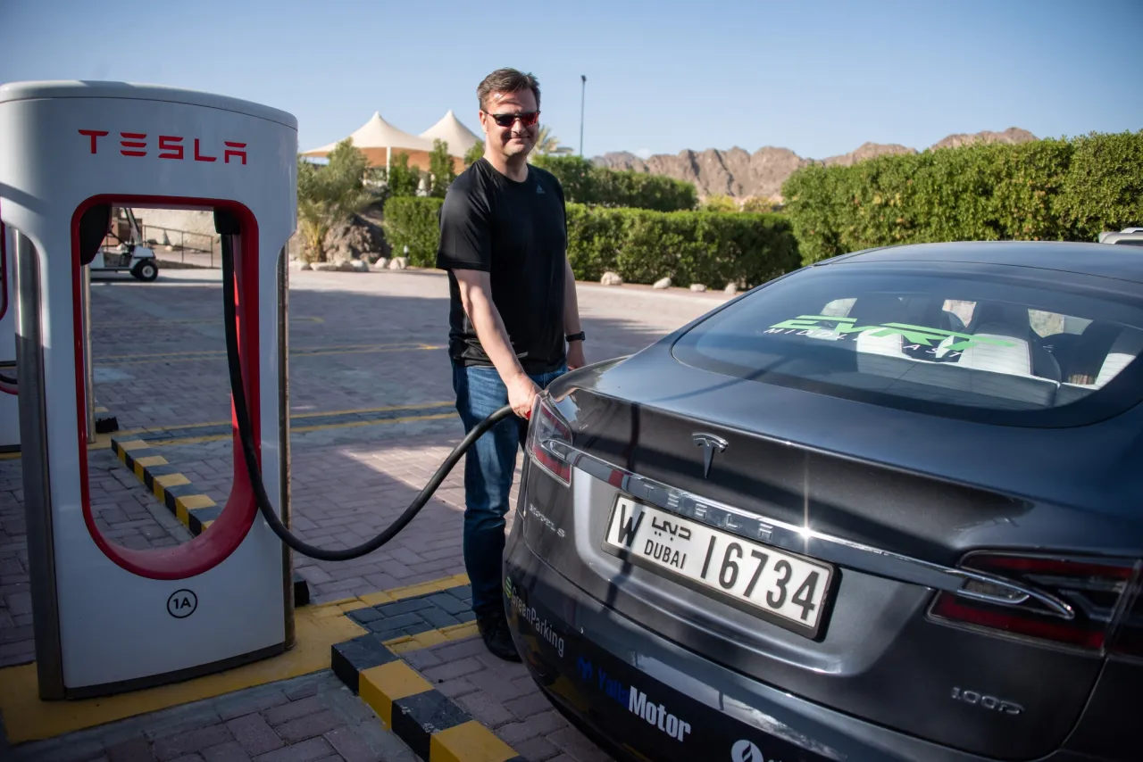 Mężczyzna ładuje Teslę na stacji Supercharger. Czas ładowania zależy od wielu czynników, ale ta stacja w Dubaju zapewnia szybkie uzupełnienie energii.