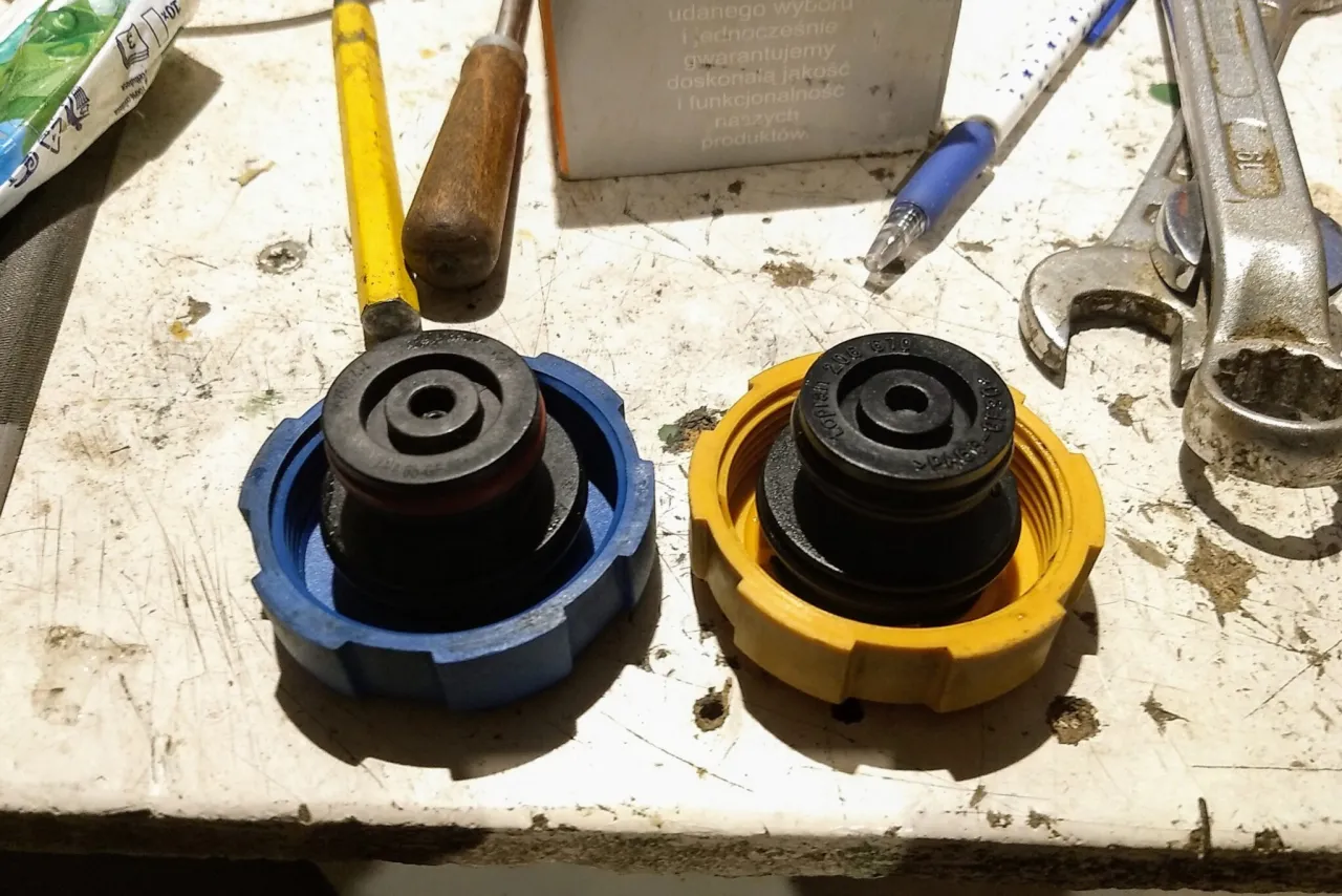 Dwa korki układu chłodzenia, niebieski i ż&oacute;łty, leżą obok narzędzi. Mogą być przyczyną wysokiego ciśnienia w układzie chłodzenia, jeśli są uszkodzone.