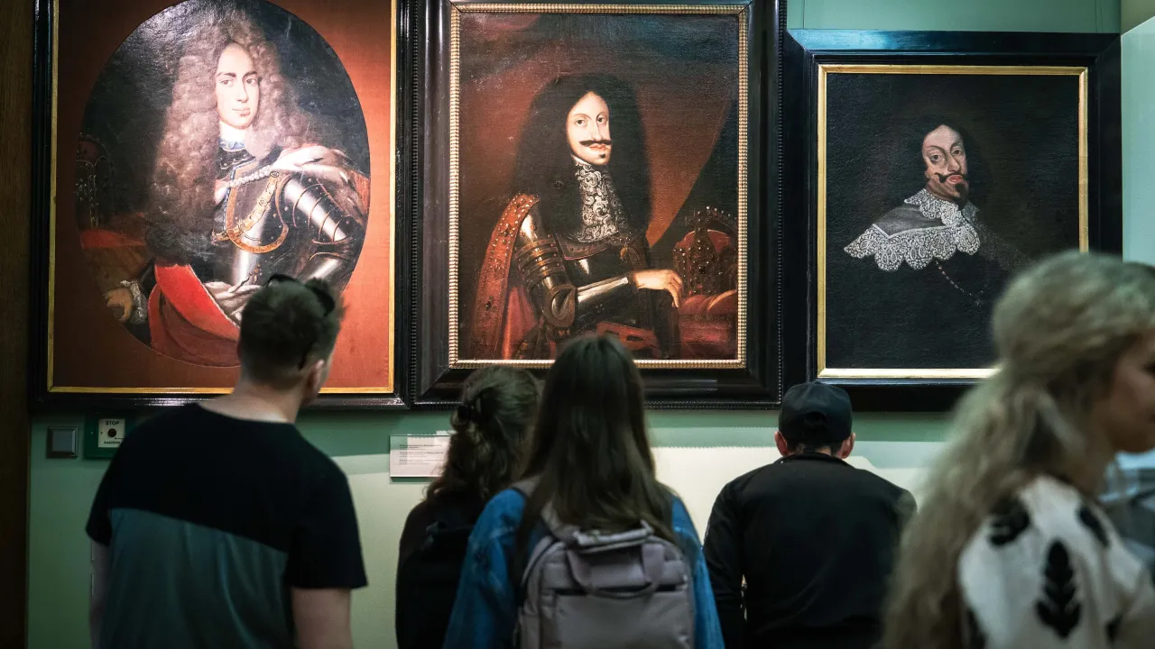 Zwiedzający podziwiają portrety w muzeach we Wrocławiu. Trzy obrazy przedstawiają mężczyzn w strojach z epoki.