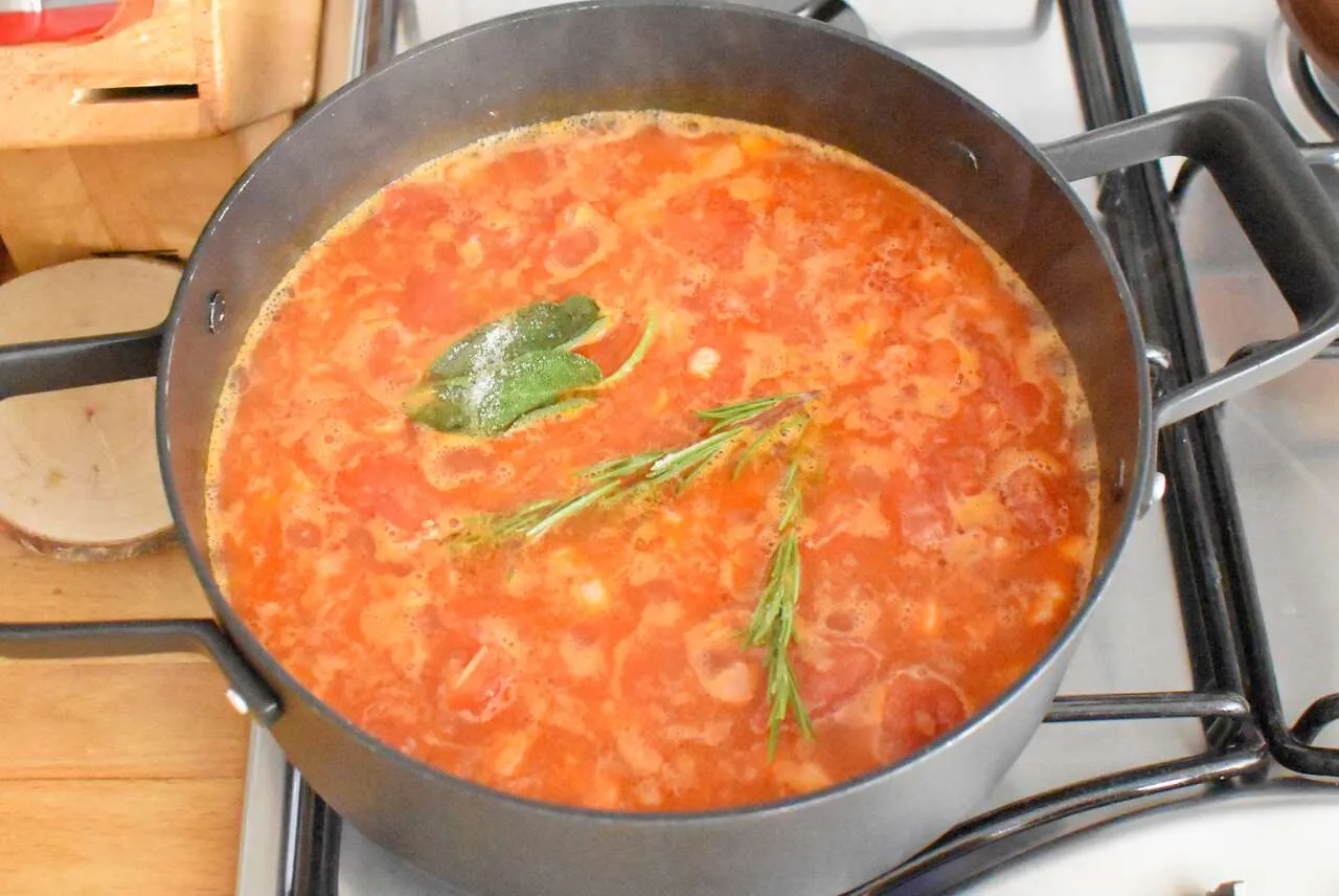 Gotowy do gotowania Pasta e Fagioli przepis. Aromatyczny bulion pomidorowy z fasolą, szałwią i rozmarynem gotuje się w garnku.