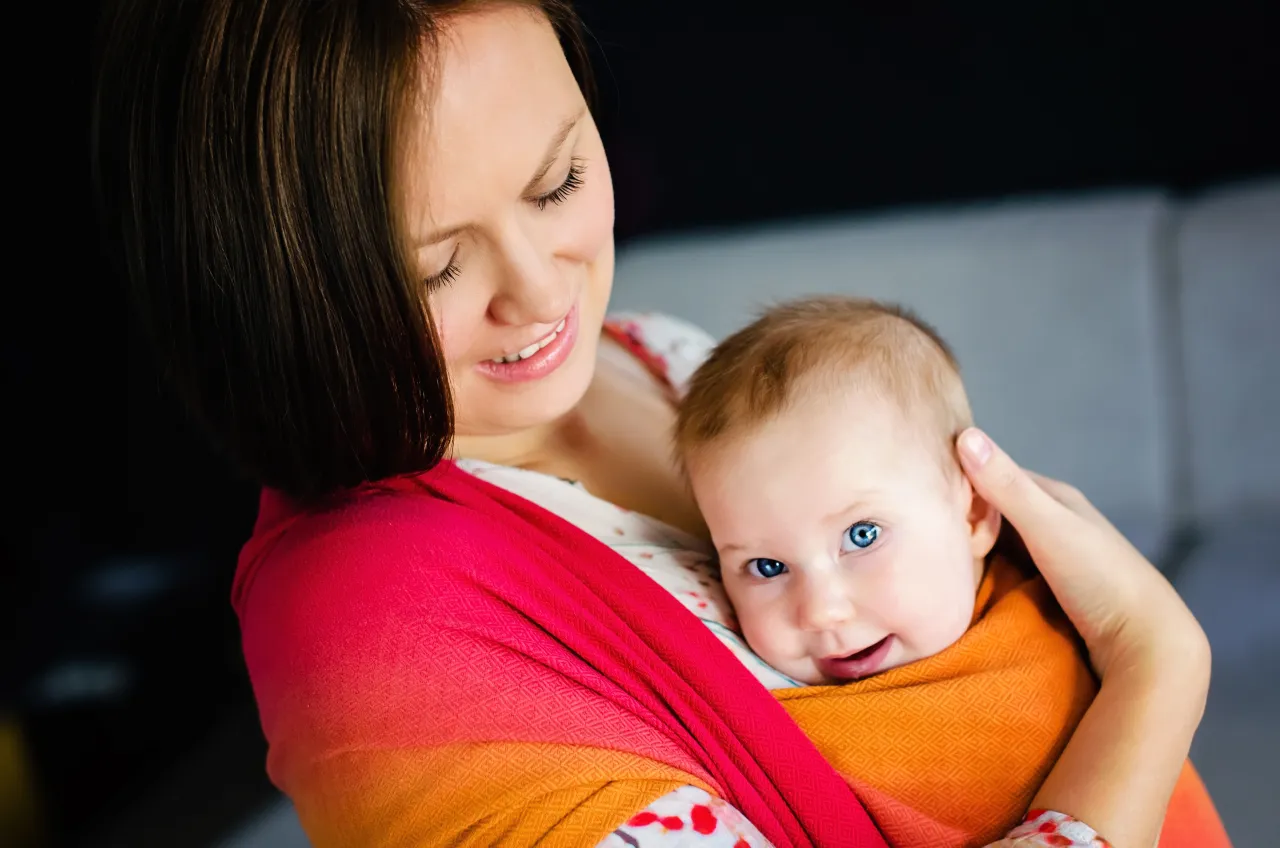 mama nosząca niemowlę w chuście w domu