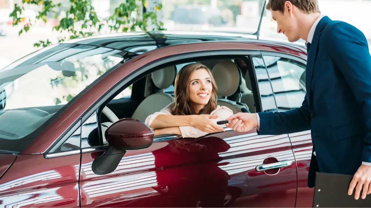 Uśmiechnięta kobieta odbiera kluczyki do samochodu, finalizując wykup z leasingu na cele prywatne.