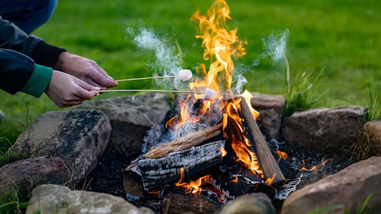 Ręce zbliżają pianki do ogniska, idealny moment, kiedy można palić ognisko na działce.