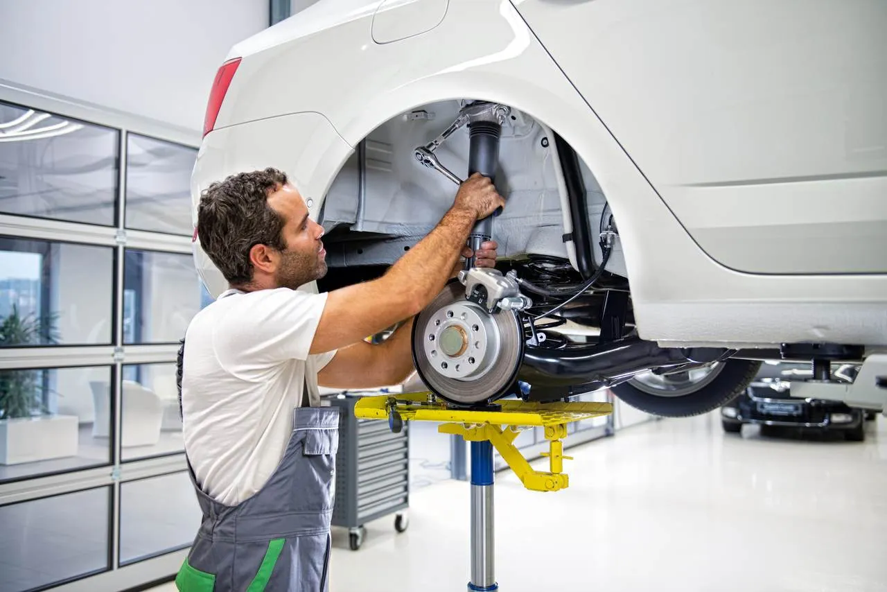 Mechanik naprawia amortyzator w białym samochodzie. To jego praca, a aso skr&oacute;t to nazwa serwisu.