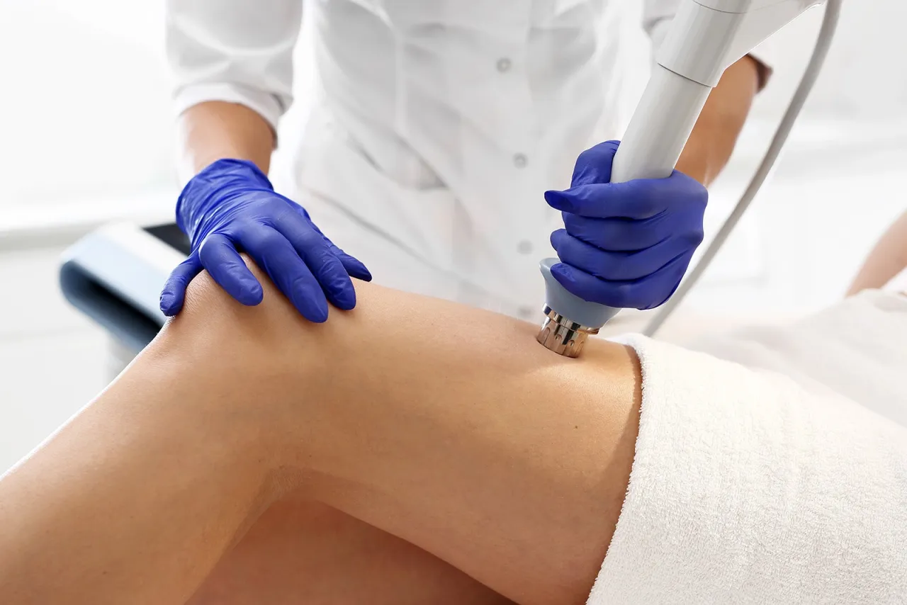 Terapeuta w niebieskich rękawiczkach stosuje laser na udo pacjentki, pokazując, jak działa laser w rehabilitacji.