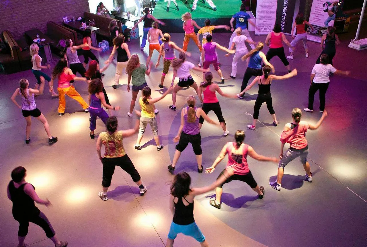 Grupa kobiet tańczy w rytm muzyki, wykonując energiczne ruchy. To właśnie co to jest zumba – połączenie tańca i fitnessu.