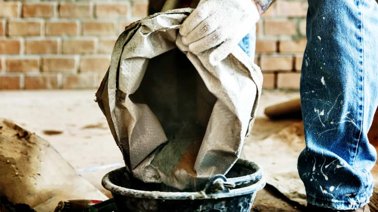Rękawica wylewa cement z worka do wiadra. Kluczowe pytanie: ile cementu na kubik betonu?