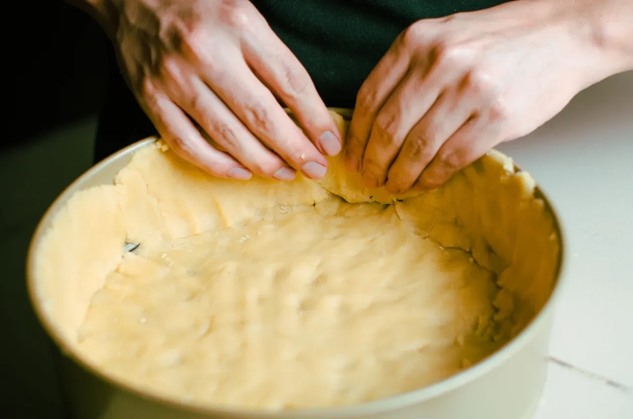 Dłonie formują kruche ciasto z mąki krupczatki w tortownicy. Idealny spód do tarty, zgodnie z przepisem.