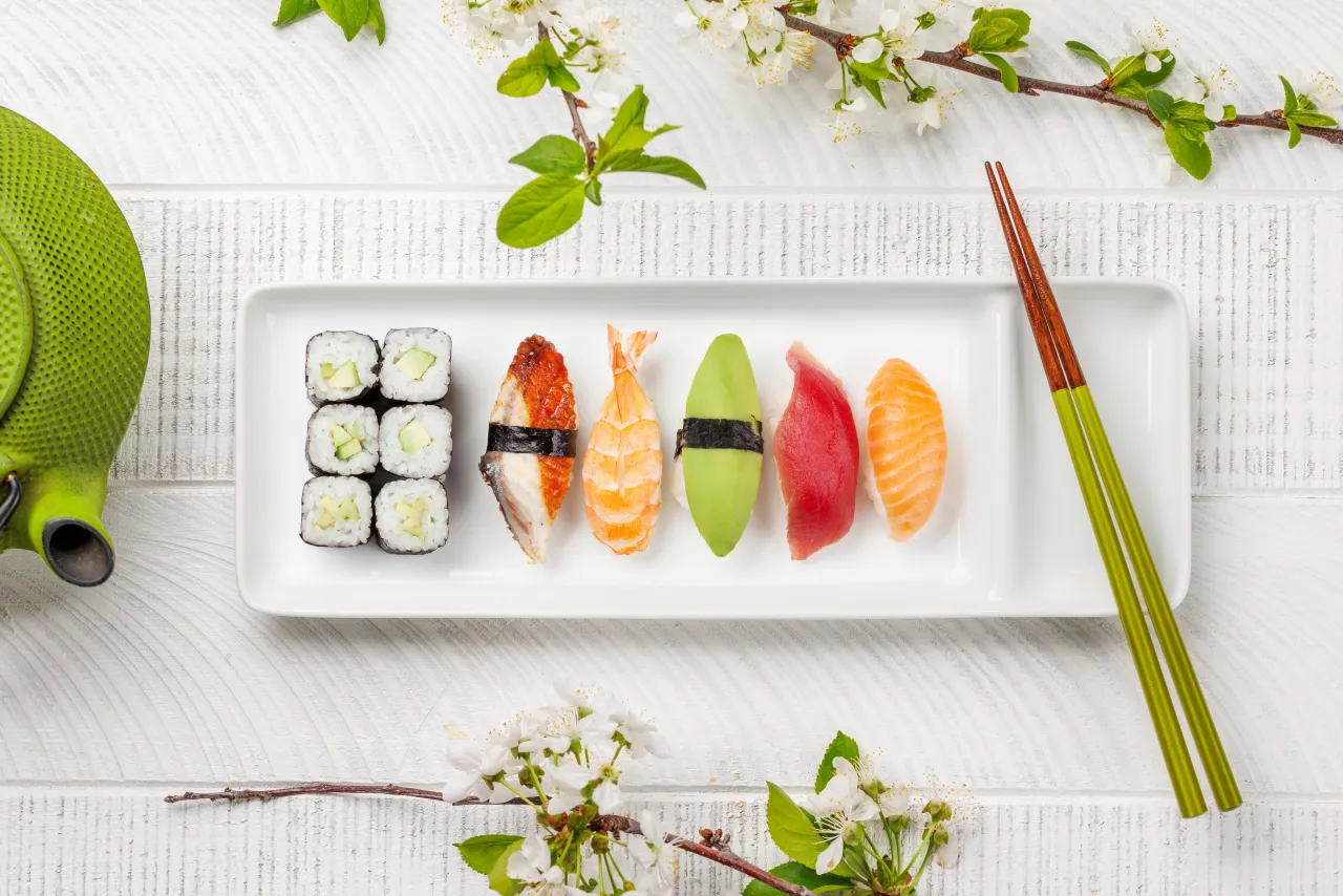 Piękny zestaw sushi, od awokado po łososia, prezentuje bogactwo kuchni japońskiej. Zielony imbryk i kwitnące gałązki dodają uroku.
