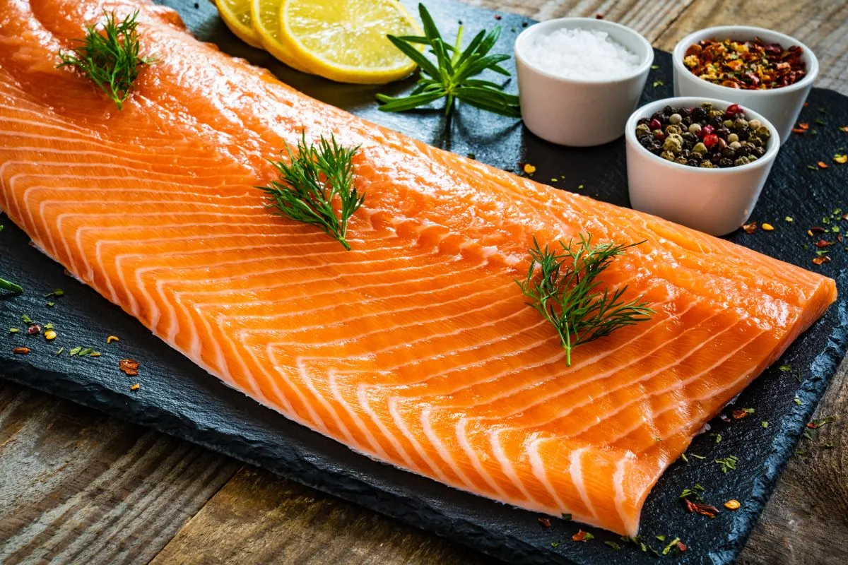 Świeży łosoś na desce z cytryną i przyprawami. Czy łososia można mrozić? Tak, aby zachować jego świeżość na dłużej.