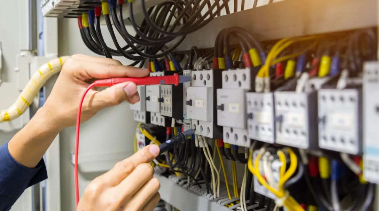 Elektryk sprawdza multimetrem małe napięcie na przewodzie neutralnym w panelu sterowania.