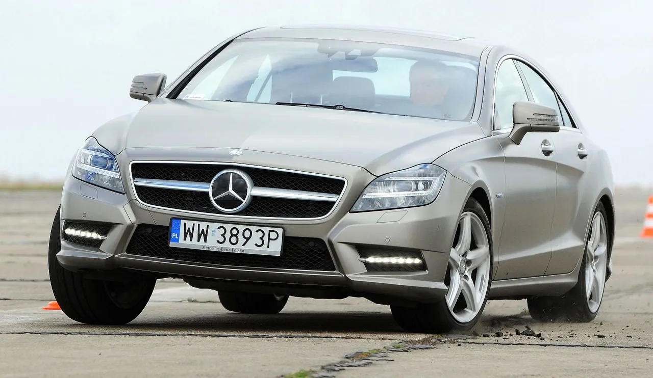 Srebrny Mercedes-Benz CLS 63 AMG na torze, z widocznym kierowcą.