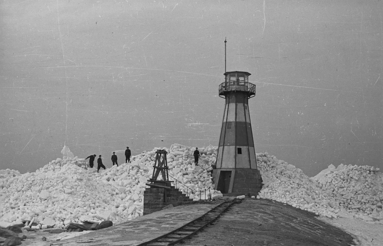 Ludzie spacerują po górach lodu, kiedy zamarzło morze bałtyckie. Latarnia morska stoi pośród lodowej pustyni.