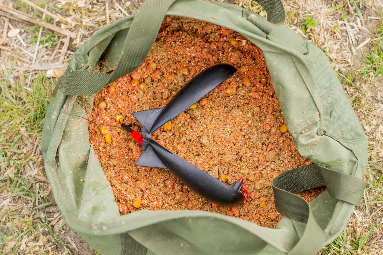 Worek z zanętą do metody, pełen drobnych ziaren i kukurydzy, z czarnym podajnikiem na wierzchu.