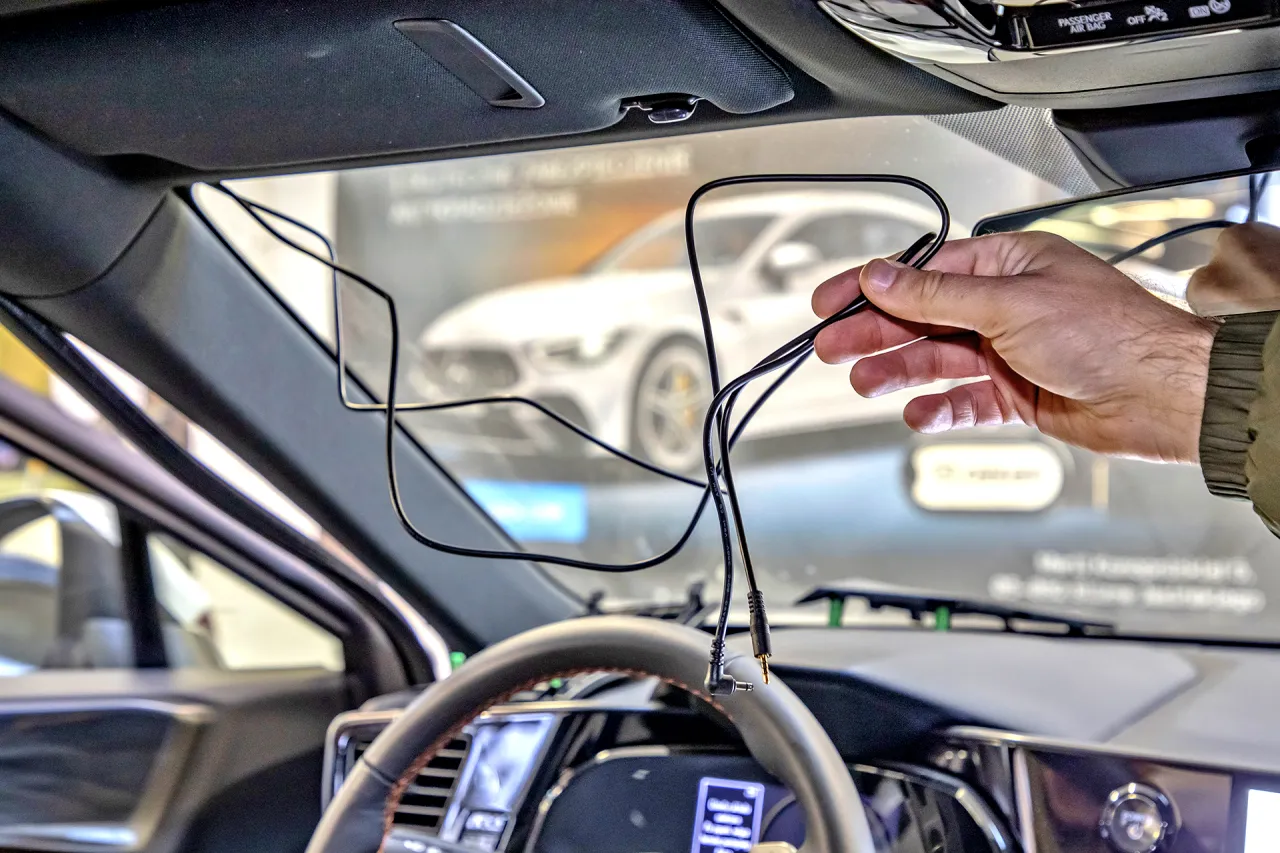 Dłoń trzyma kable do wideorejestratora, pokazując, jak zamontować urządzenie w samochodzie.