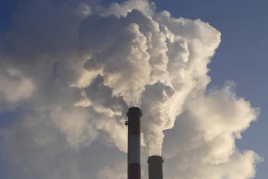 telefon kom&oacute;rkowy w dłoni robiący zdjęcie dymiącego komina