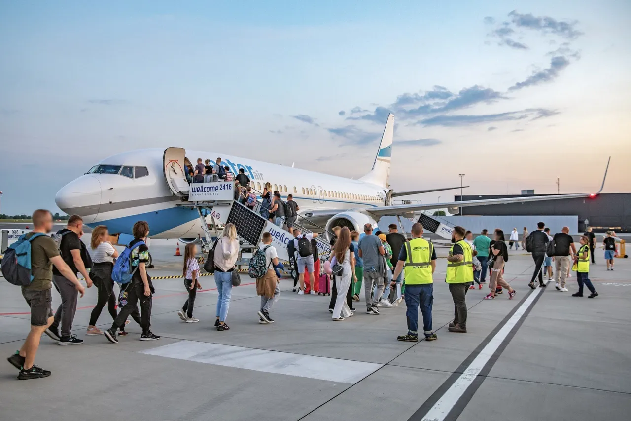 Pasażerowie wsiadają do samolotu na lotnisku Radom. Widać schody i obsługę lotniska. Jakie linie latają z Radomia?