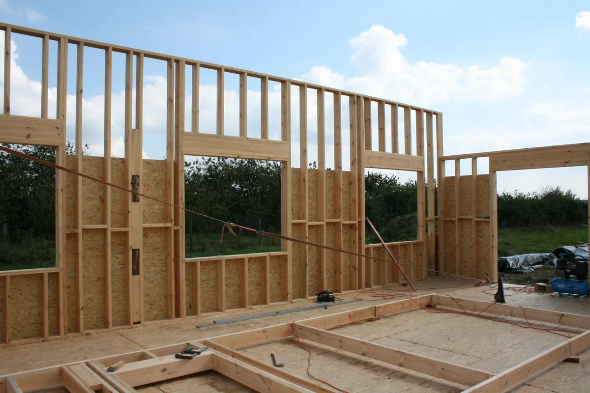 Szkielet domu drewnianego w budowie. Widoczne ściany z belek, otwory okienne i drzwiowe, podłoga z płyt OSB. To początek, jak zrobić konstrukcje domku drewnianego.