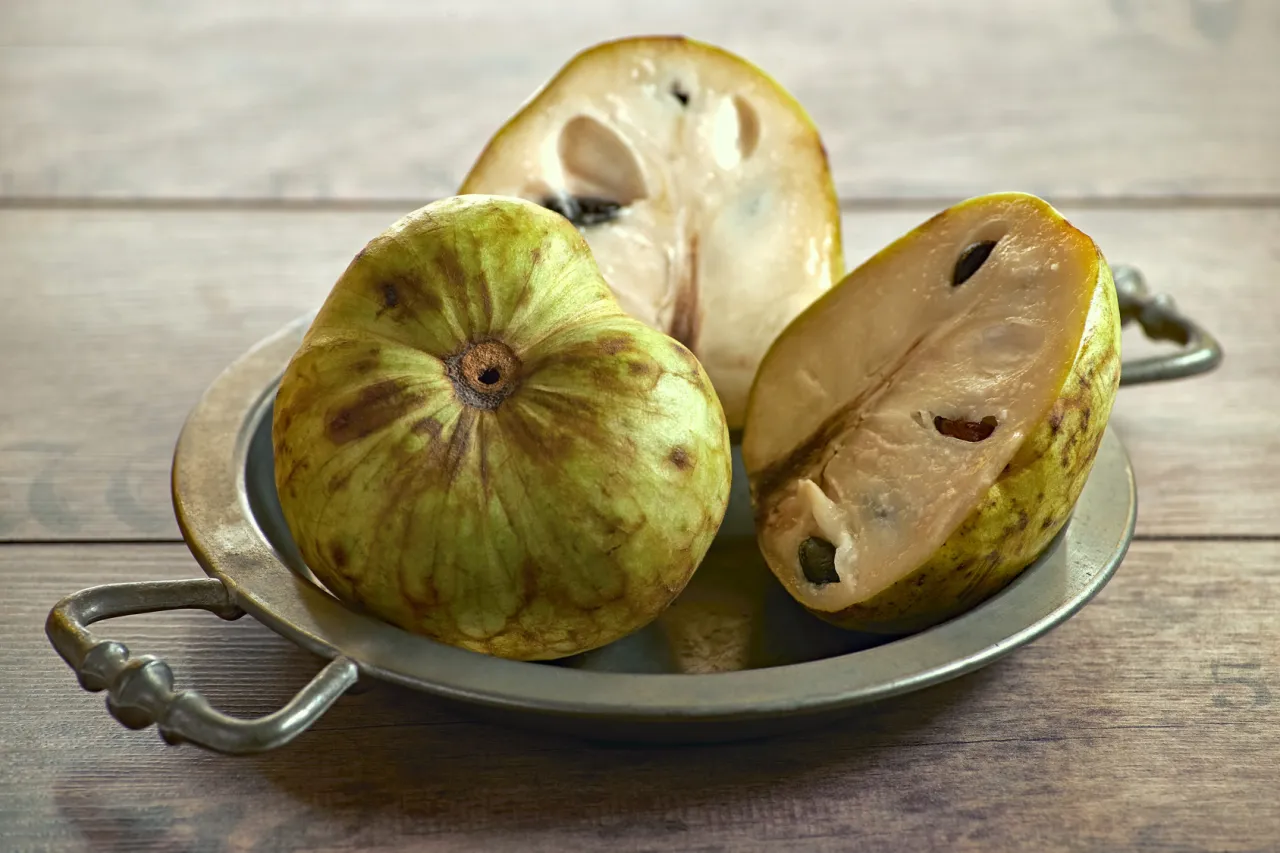 Cała i przekrojona cherimoya na metalowej tacce. Owoc kusi swoim egzotycznym, słodkim smakiem.