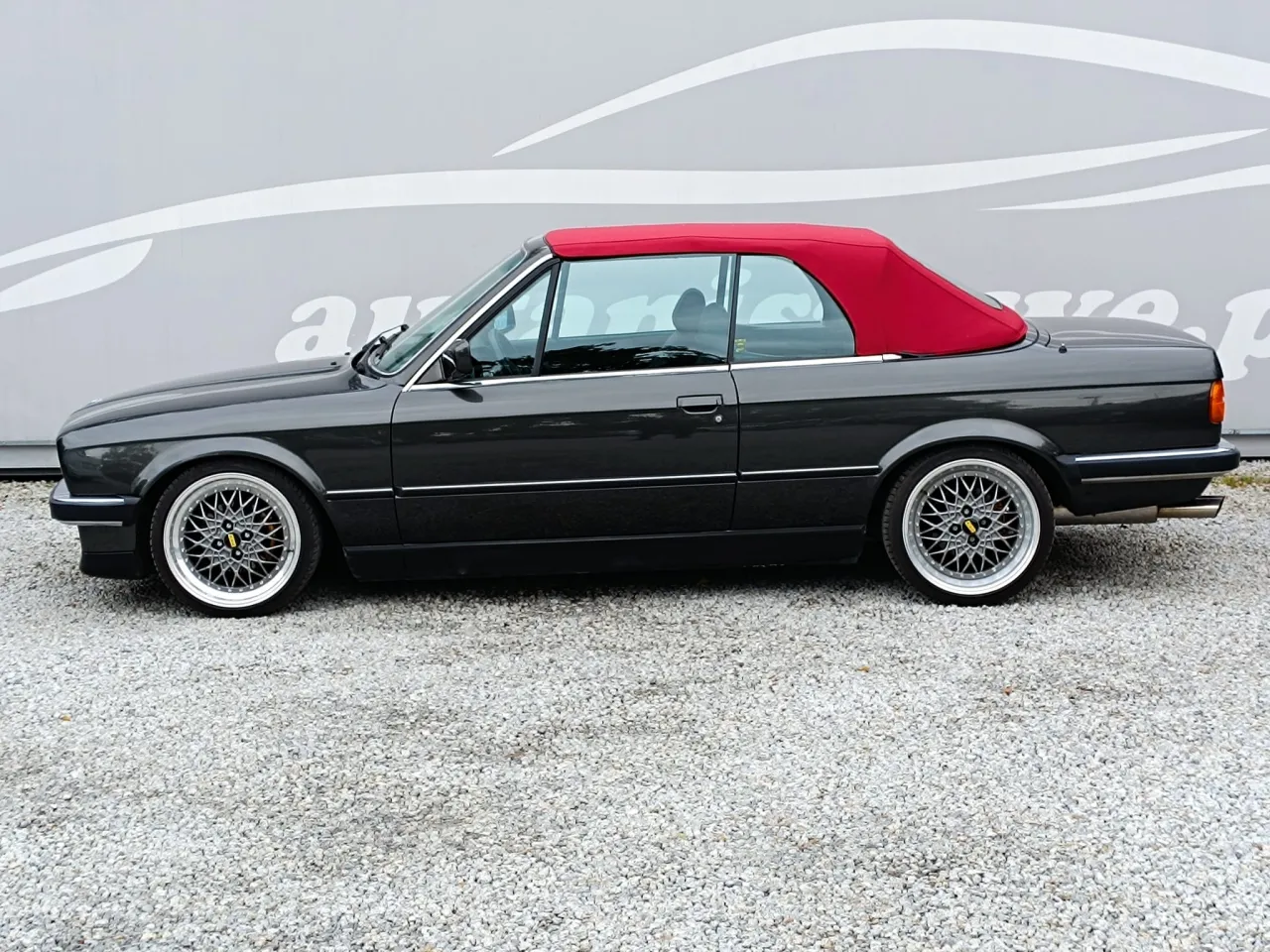 Klasyczne bmw e30 cabrio z czerwonym dachem, zaparkowane na żwirze.