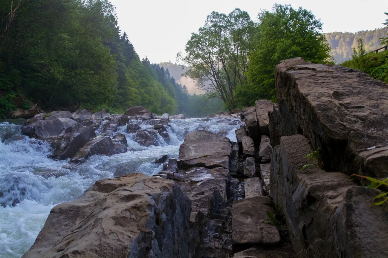Wodospady i kamienie w rezerwacie przyrody Sine Wiry. Woda spływa po skałach, otoczona zielonymi lasami.
