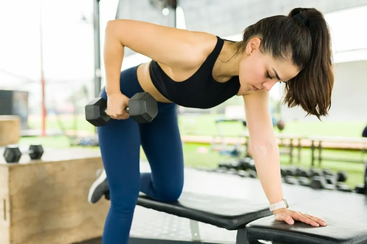 Kobieta ćwiczy z hantlem na ławce. Zastanawiasz się, ile ćwiczyć dziennie, by osiągnąć takie rezultaty?